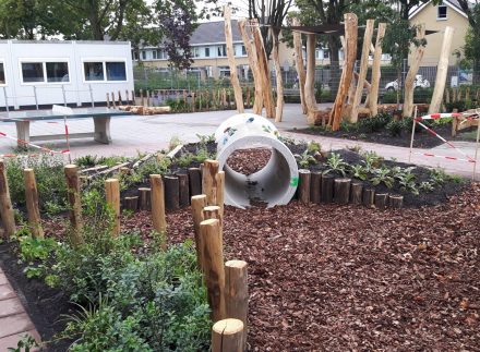 Speeltoestellen geïntegreerd in groen schoolplein.