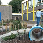 Speeltoestellen geïntegreerd in groen schoolplein.