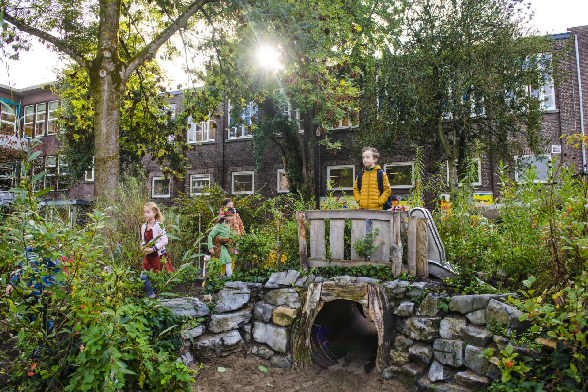 Speeltoestellen geïntegreerd in een groen schoolplein met tunnels, glijbanen en bruggen.